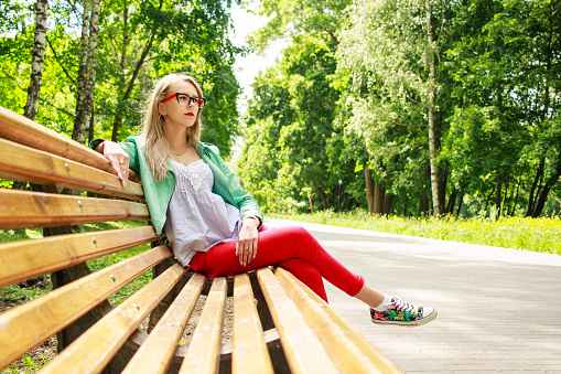 cute girl in jeans and a jacket is sitting on a park bench