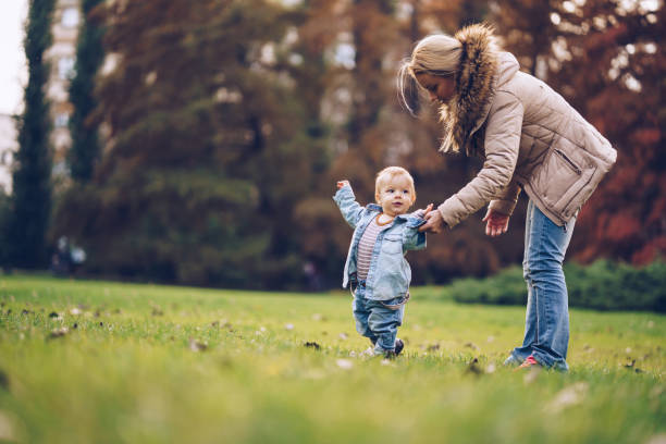 istock Small boy taking first steps with help of his mother in autumn park. 973162412