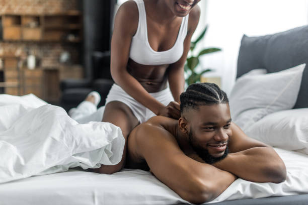 cropped image of african american girlfriend doing massage for boyfriend in bedroom - african descent sex symbol couple sensuality imagens e fotografias de stock
