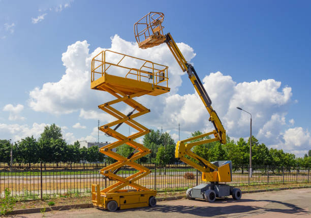 Self propelled wheeled articulated boom lift and scissor lift Yellow self propelled articulated boom lift and scissor lift on background of street with trees and sky mobile crane stock pictures, royalty-free photos & images