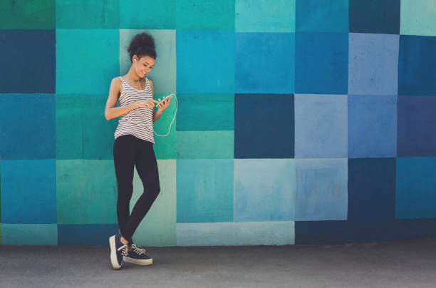 African-american woman posing, leaning on bright wall Happy smiling african-american woman leaning on bright blue graffiti wall, while listening music, relaxing from jog training, copy space leaning stock pictures, royalty-free photos & images