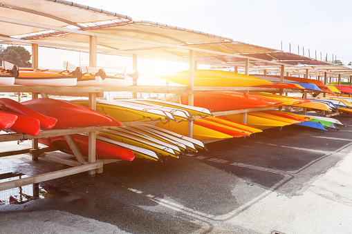 In sunlight, red, yellow and white kayaks placed upside down on metal storage racks. Stocked canoe in the Brest, France 28 May 2018.