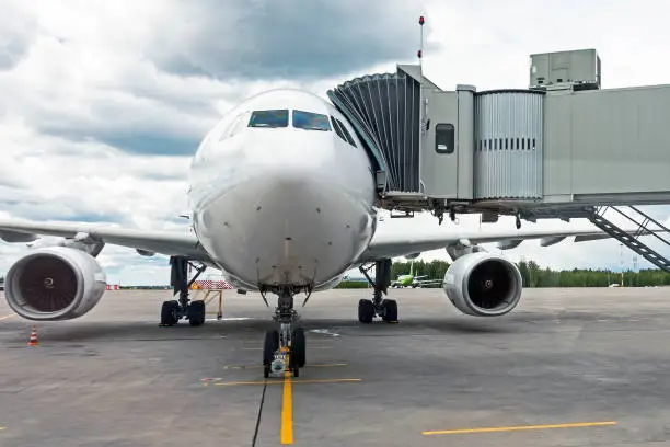 Commercial passenger airplane in the parking at the airport with a nose forward and a gangway - front view