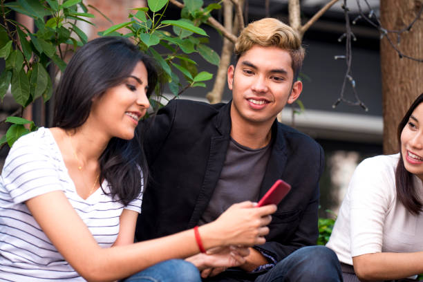 istock Young Asian friend sitting outdoors and using their mobile phones 973198882