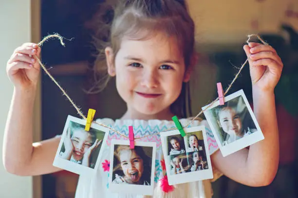 Four years old little girl holding string of instant photos