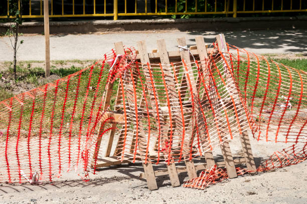 istock Improvised road construction site barrier with protective caution orange fence or net to protect street reconstruction work ahead 973255274