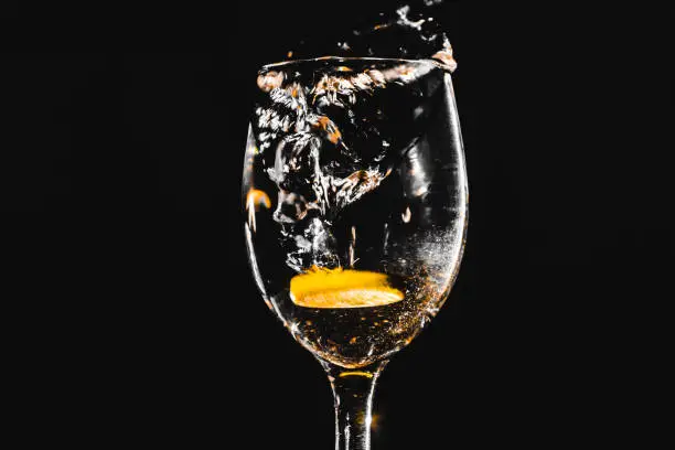 Pure water splashing from the pure elegant wineglass standing against black background