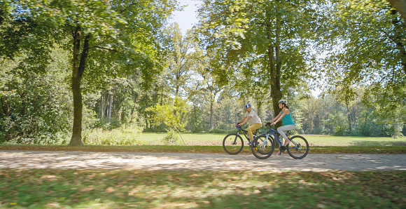 Mid adult couple riding bicycle in park.