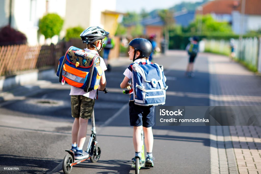 Zwei School kid jungen in Schutzhelm mit Roller in der Stadt mit Rucksack an sonnigen Tag Reiten. Glückliche Kinder in bunten Kleidern, Radfahren am Weg zur Schule. - Lizenzfrei Kind Stock-Foto