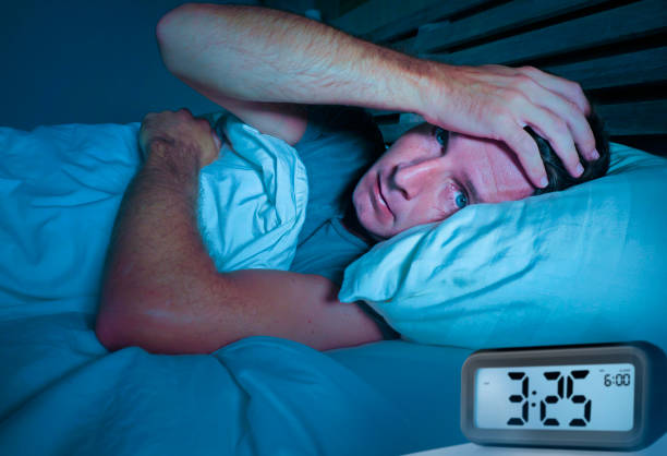 istock worried sad young attractive man awake lying sleepless on bed with eyes wide opened suffering insomnia sleeping disorder depressed and thoughtful with alarm clock pointing late night hour 973262382