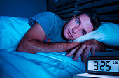 restless worried young attractive man awake at night lying on bed sleepless with eyes wide opened suffering insomnia sleeping disorder depressed and sad in rest privation stress concept