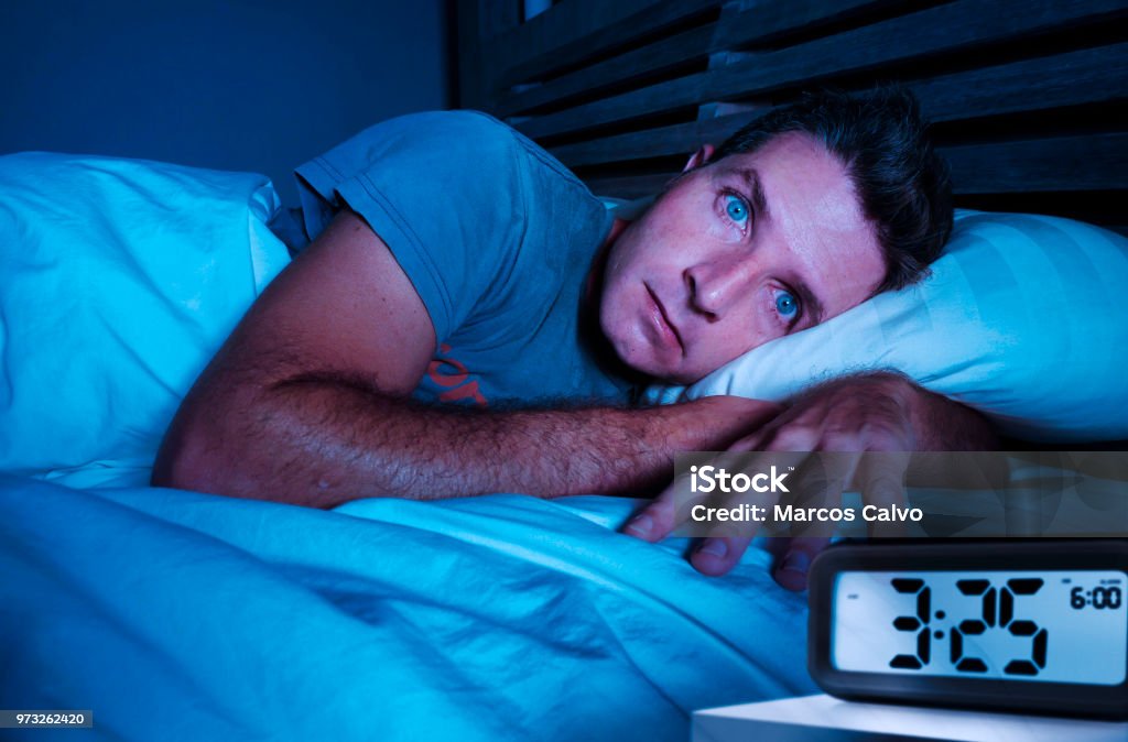 restless worried young attractive man awake at night lying on bed sleepless with eyes wide opened suffering insomnia sleeping disorder depressed and sad in rest privation stress concept Insomnia Stock Photo