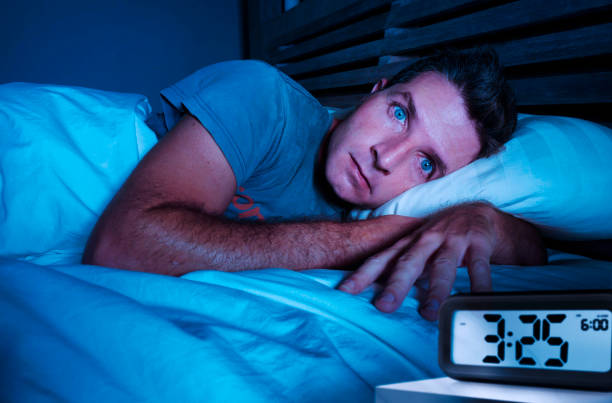 restless worried young attractive man awake at night lying on bed sleepless with eyes wide opened suffering insomnia sleeping disorder depressed and sad in rest privation stress concept stock photo