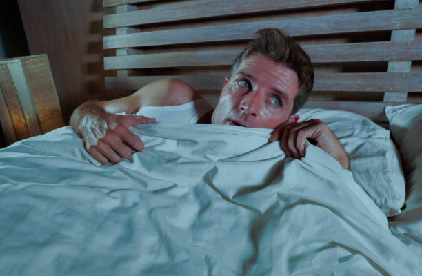 istock sleepless young man lying in bed stressed and scared suffering nightmare and horror bad dream grabbing duvet frightened and paranoid in sleeping disorder and resting problem lifestyle concept 973263240