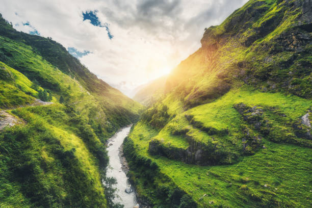 istock View with amazing mountains covered green grass, river, meadows and forest, blue sky with clouds, sun in autumn in Nepal at sunset. Mountain valley at bright sunny evening. Travel in Himalayas. Nature 973270094