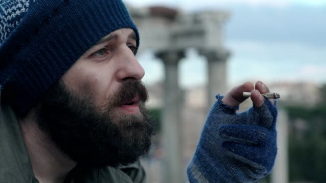 sad and thoughtful homeless man lighting a cigarette