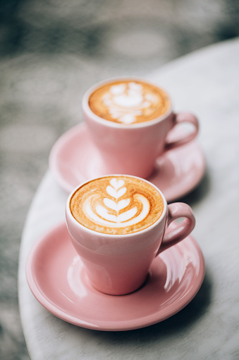 Two beautiful pink cups of cappuccino with latte art on the table.