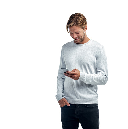 Studio shot of a handsome young man using his cellphone while standing against a white background