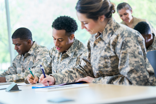 Male and female cadets concentrate while taking an exam in class. They are attending a military academy.