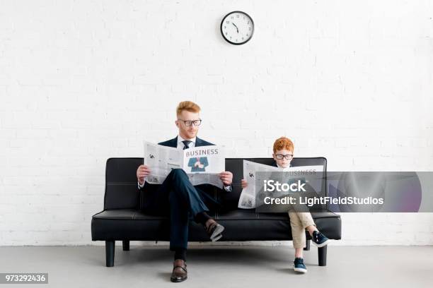 Father And Son Businessmen Wearing Eyeglasses And Reading Newspapers On Sofa Stock Photo - Download Image Now