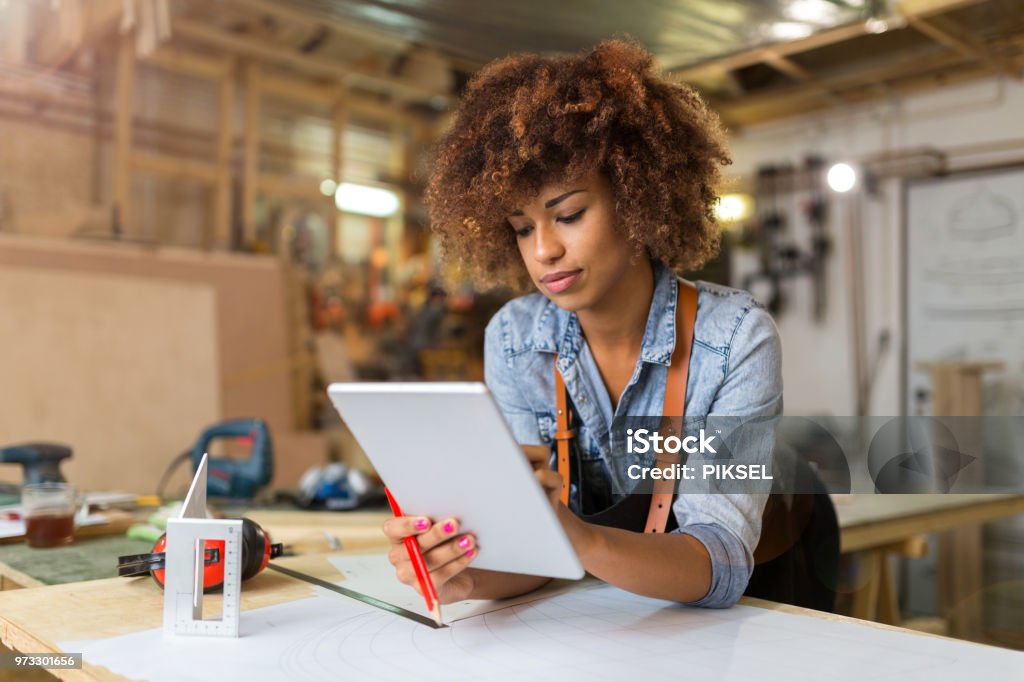 Young woman using a tablet in her workshop Afro american woman craftswoman working in her workshop Small Business Stock Photo