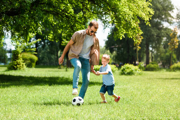 padre e hijo jugando al fútbol en el parque - ball horizontal outdoors childhood fotografías e imágenes de stock