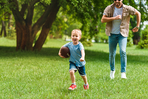 happy father and son running with american football ball at park