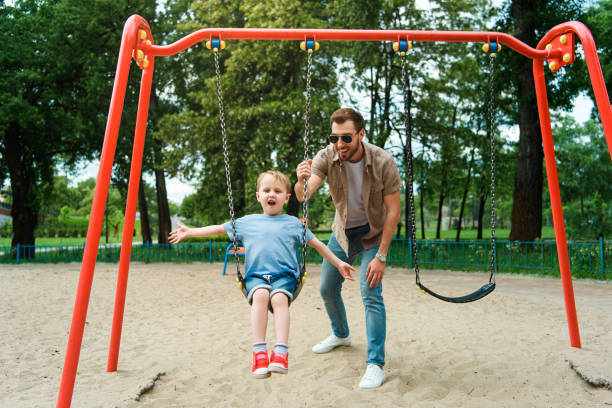 istock father and son having fun on swing at playground in park 973324976