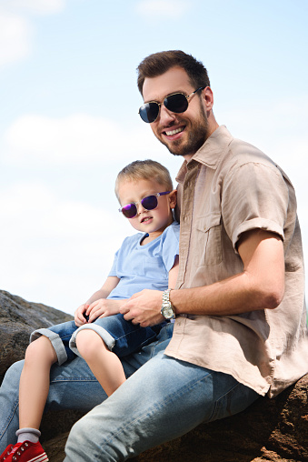 happy father and son in sunglasses looking at camera at park