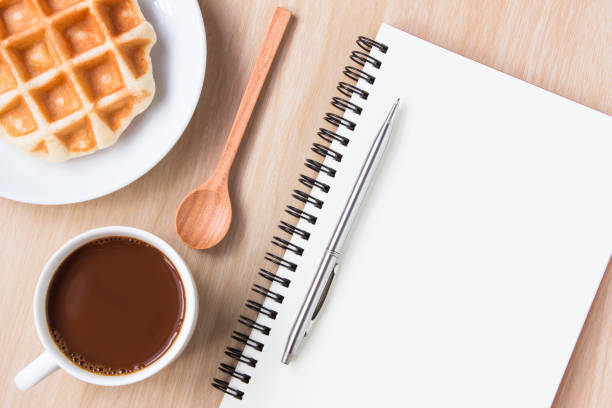 istock Blank paper and , coffee on wood table background / Open blank white paper notebook with copy space and a pen lying on a white desk / can be used for your text or artwork / top view 973325978