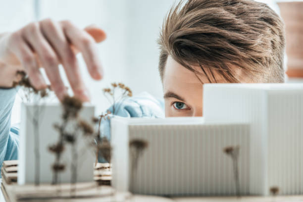 partial view of young architect looking at self made building model in office