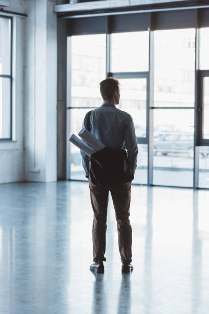 istock back view of architect with bag full of blueprints standing in empty building 973342688