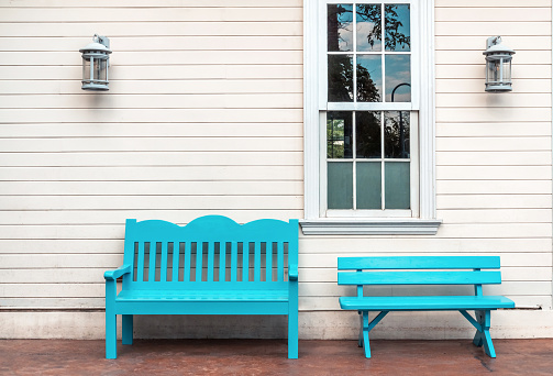 two Light blue wooden bench and a window. White wall.