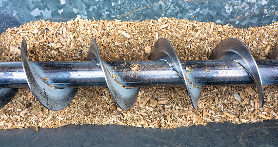 A metal auger for loading wood chips from a storage hopper into a biomass boiler.
