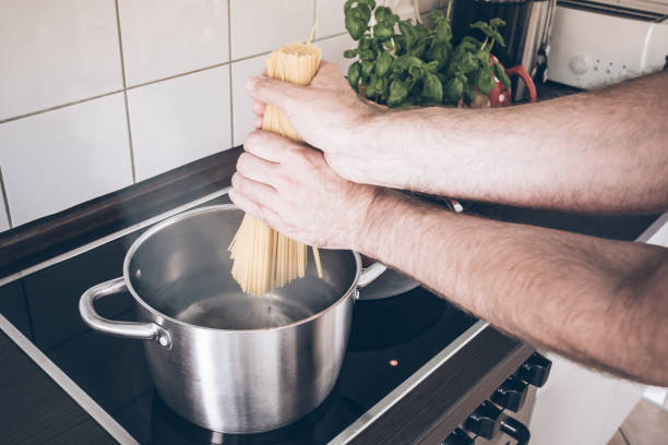 istock hands putting spaghetti in pot with boiling water on stove 973357648