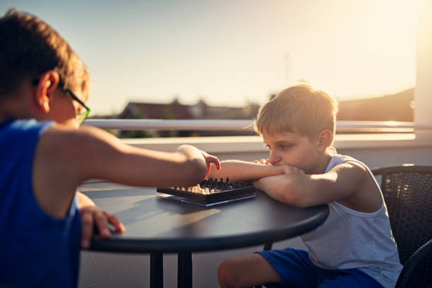 Two little boys are enjoying a game of chess on the balcony. Setting sun is backlighting the scene.\nNikon D850