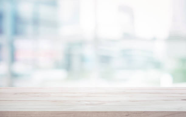 istock Wood table top on blur white glass window background form office building 973364316
