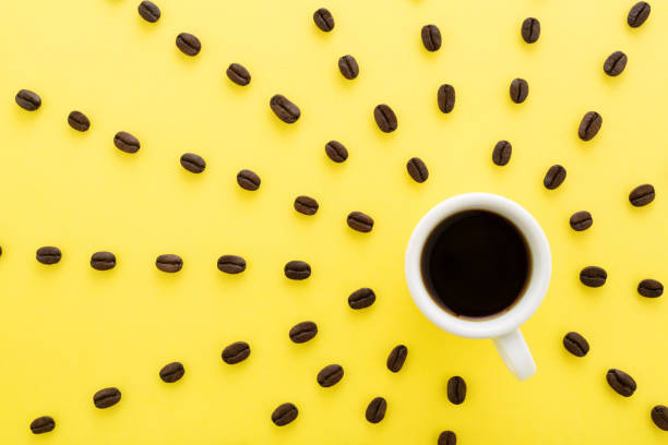Black Coffee with sun rays of coffee beans on pastel yellow background. Cup of coffee espresso with sun rays of coffee beans on yellow background. Flat lay, creative design. Sunny morning & black coffee concept. pop art photos stock pictures, royalty-free photos & images