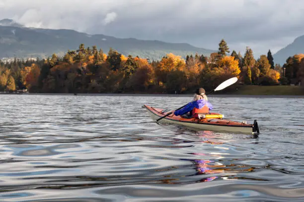 Adventurous girl is kayaking during a sunny sunrise in front of Stanley Park during Autumn Season. Taken in Vancouver, British Columbia, Canada.