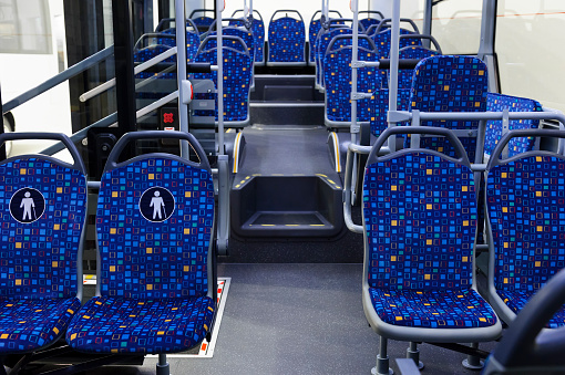Bus inside, city transportation interior with blue seats in row, retirement places, open doors, handles for standing passengers