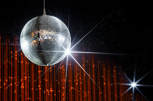 Party disco ball with stars in nightclub with striped orange and black walls lit by spotlight, nightlife entertainment industry