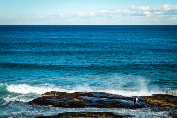 An Australian surfer confidently walks to the water, ready to make his entry into the winter surf. Taken on the Bondi Beach to Coogee Beach walk in Sydney, Australia.