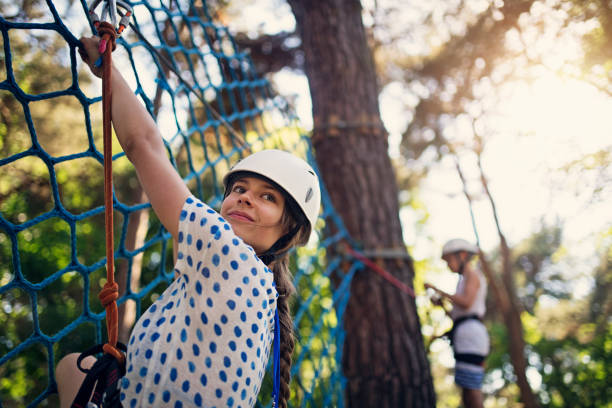Kids having fun during in ropes course  adventure park Kids during ropes course in and adventure park. The girl is climbing on net and the boy is attaching a carabiner in the background.
Sunny summer day.
Nikon D850 canopy tour photos stock pictures, royalty-free photos & images