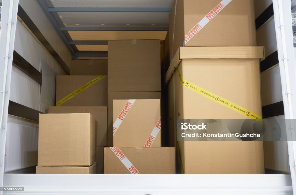 In the cargo area of the truck View of the cargo area of light commercial vehicle. Russian text on yellow adhesive tape of the box: First class mail. Russian red text on the white adhesive tape: Fragile. Box - Container Stock Photo