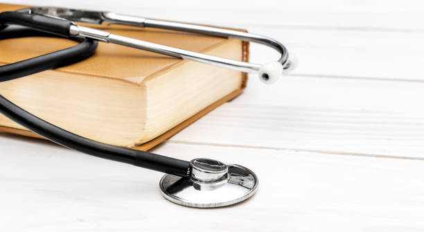 istock Stethoscope with book on white wooden table. Close up. 973432134