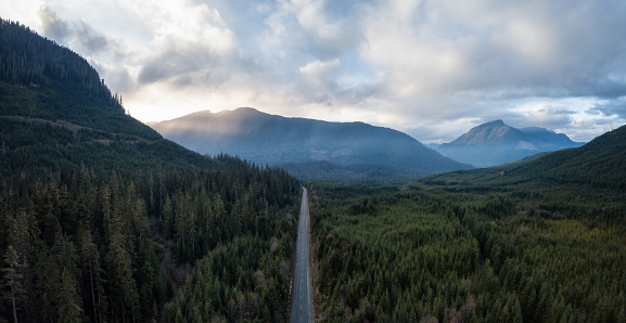 Aerial panoramic drone view of a scenic highway by the beautiful Canadian Landscape covered in clouds and fog. Taken in Vancouver Island, British Columbia, Canada.