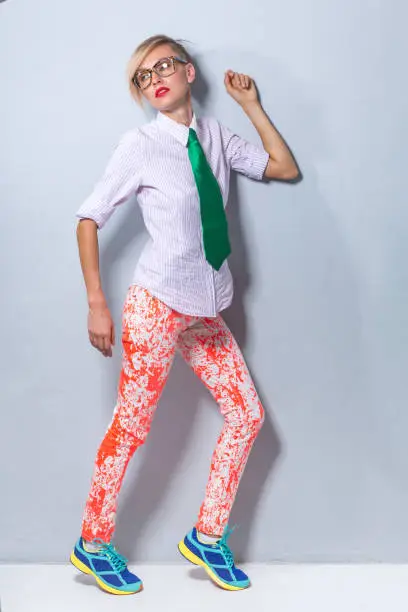 Fashion portrait of stylish blonde girl in trendy clothes, wearing green tie, shirt and bright pants isolated over light background. Full length
