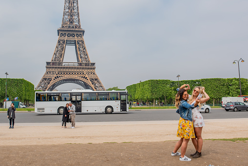 Paris / France - May 15, 2018: Young women friends pose together for a selfie in the Champs du Mars park, in front of the famous, iconic Eiffel Tower.
