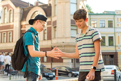 Front view of teenage boys in t-shirts, shorts, and backpacks smiling and communicating as they walk side by side. Part of lifestyle series depicting deaf family and friends.