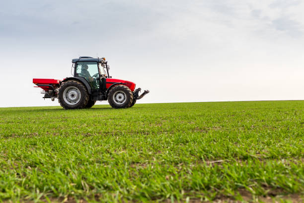 istock Farmer in tractor fertilizing wheat field at spring with npk 973478574